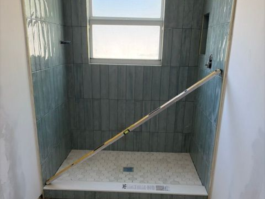 Small tiled shower stall with a window and a grab bar across the back wall.
