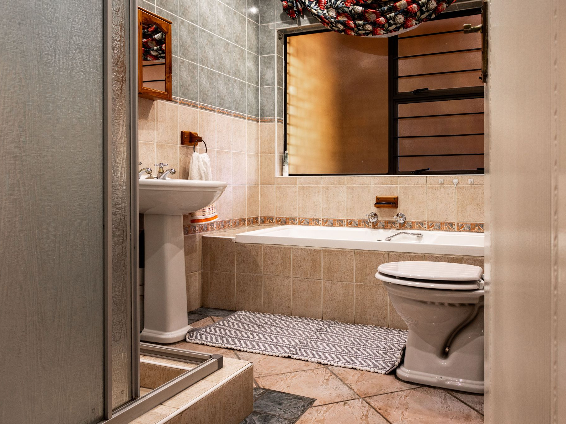 Small bathroom with a sink, bathtub, and toilet, featuring beige tile and a large mirror.