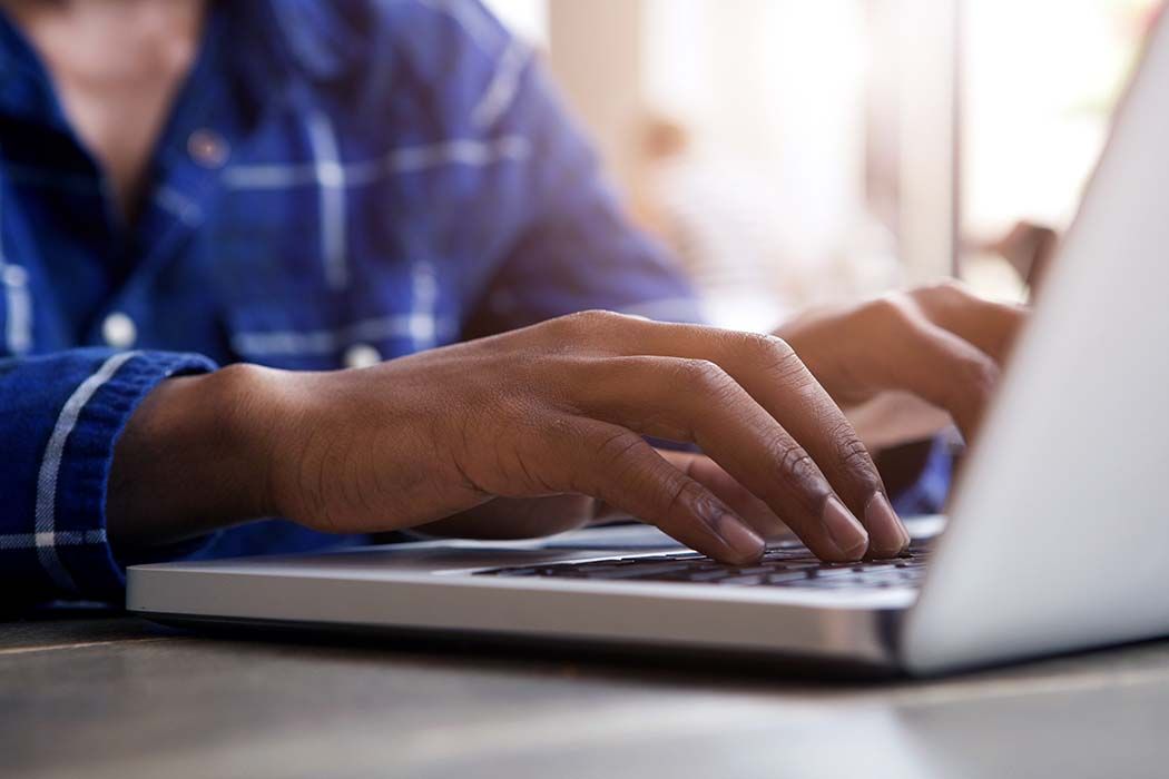 Person typing on a laptop in a blue plaid shirt