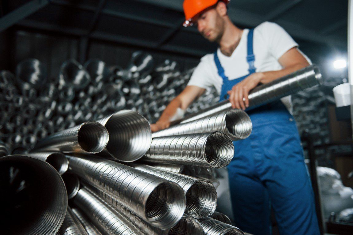 A man in a hard hat is standing next to a pile of metal pipes.