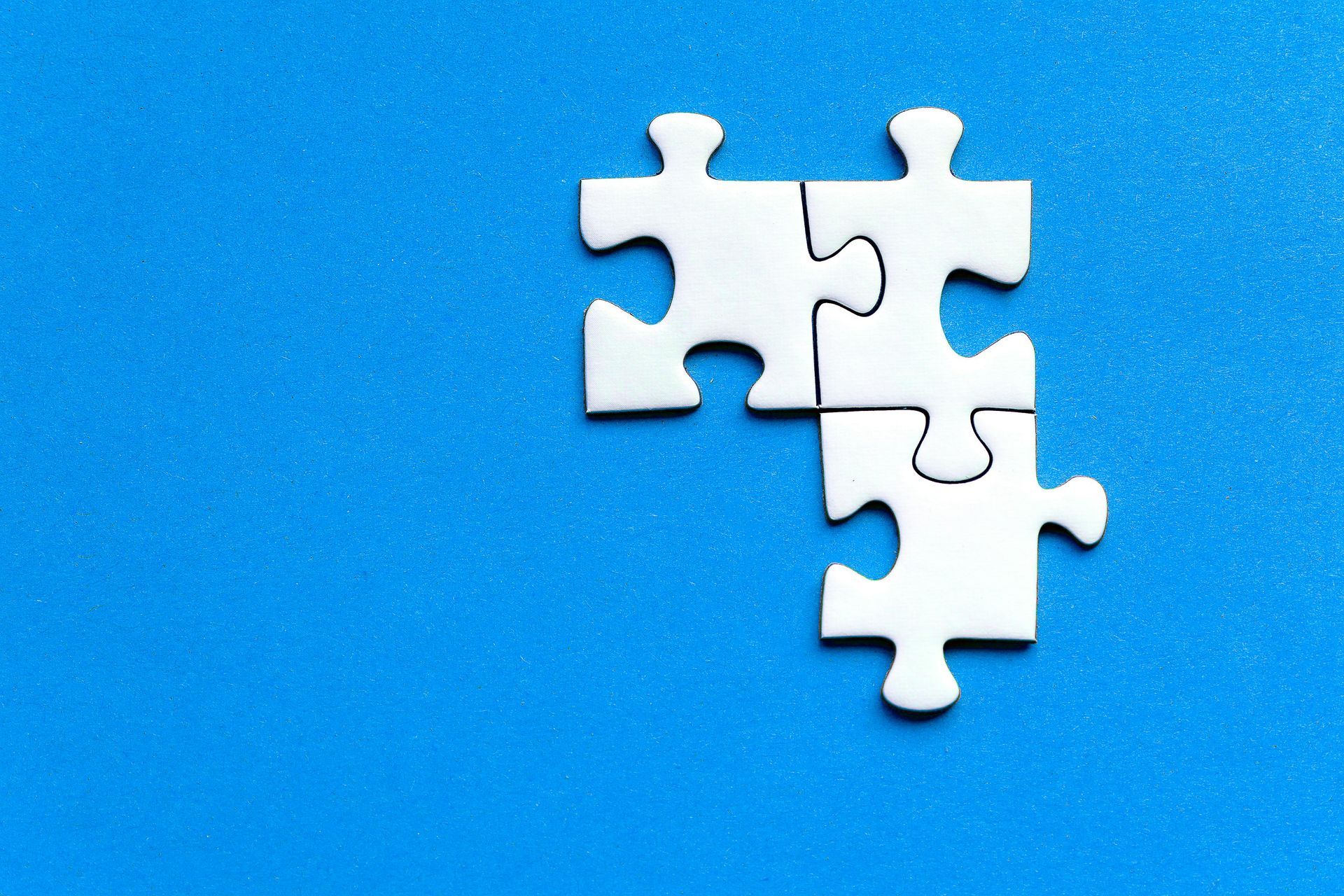 Three white puzzle pieces are sitting on top of each other on a blue surface.