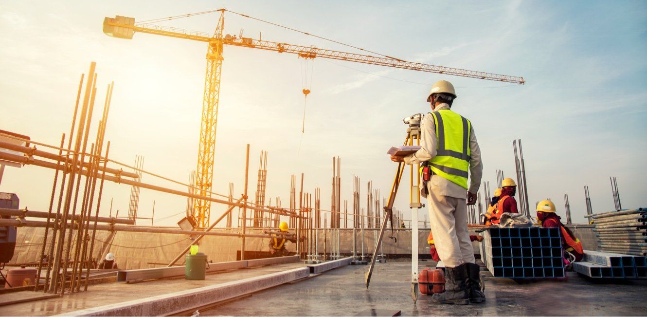 A construction worker is standing on a construction site with a crane in the background.