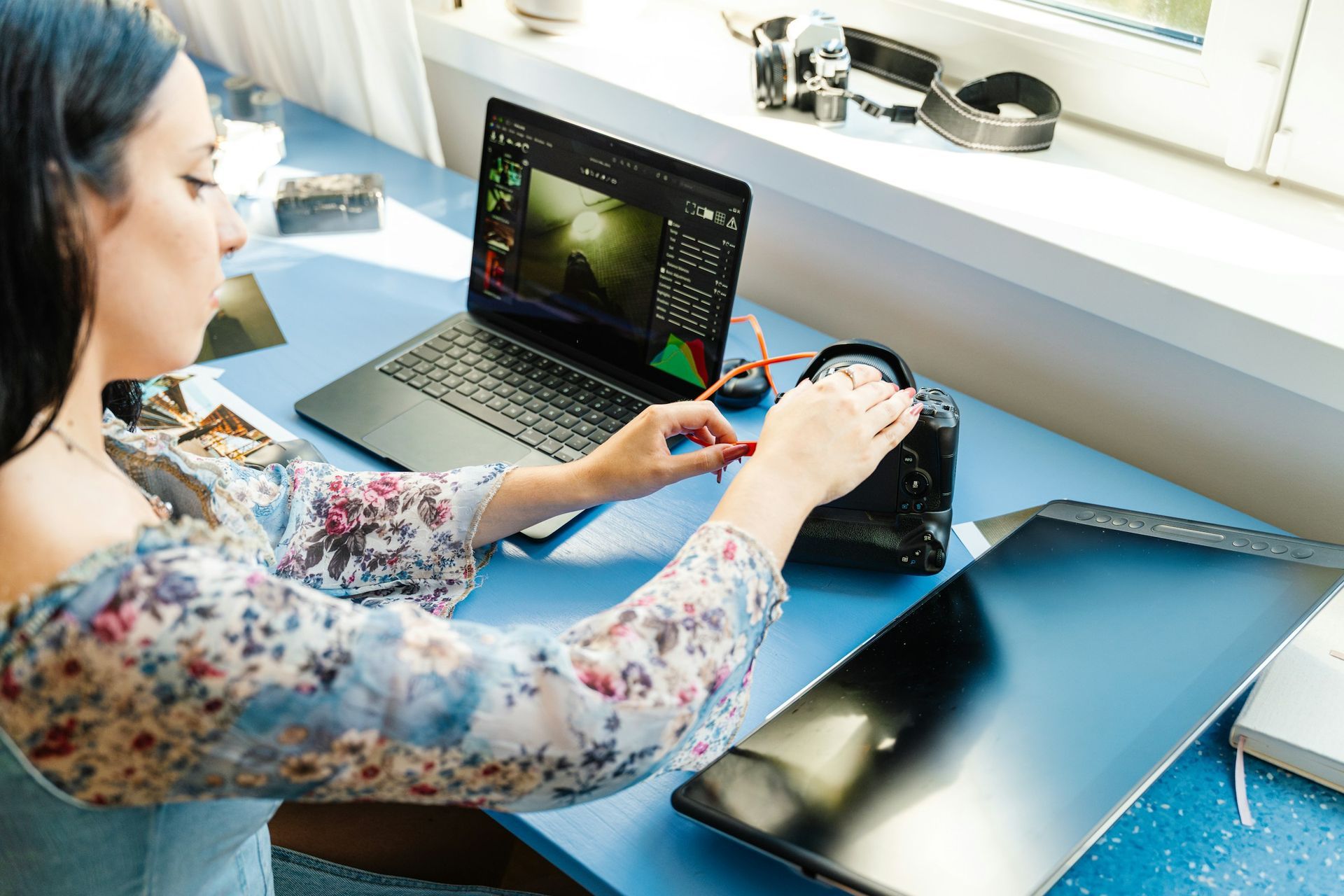 Woman connecting a camera to a laptop for digital content creation and editing workflow
