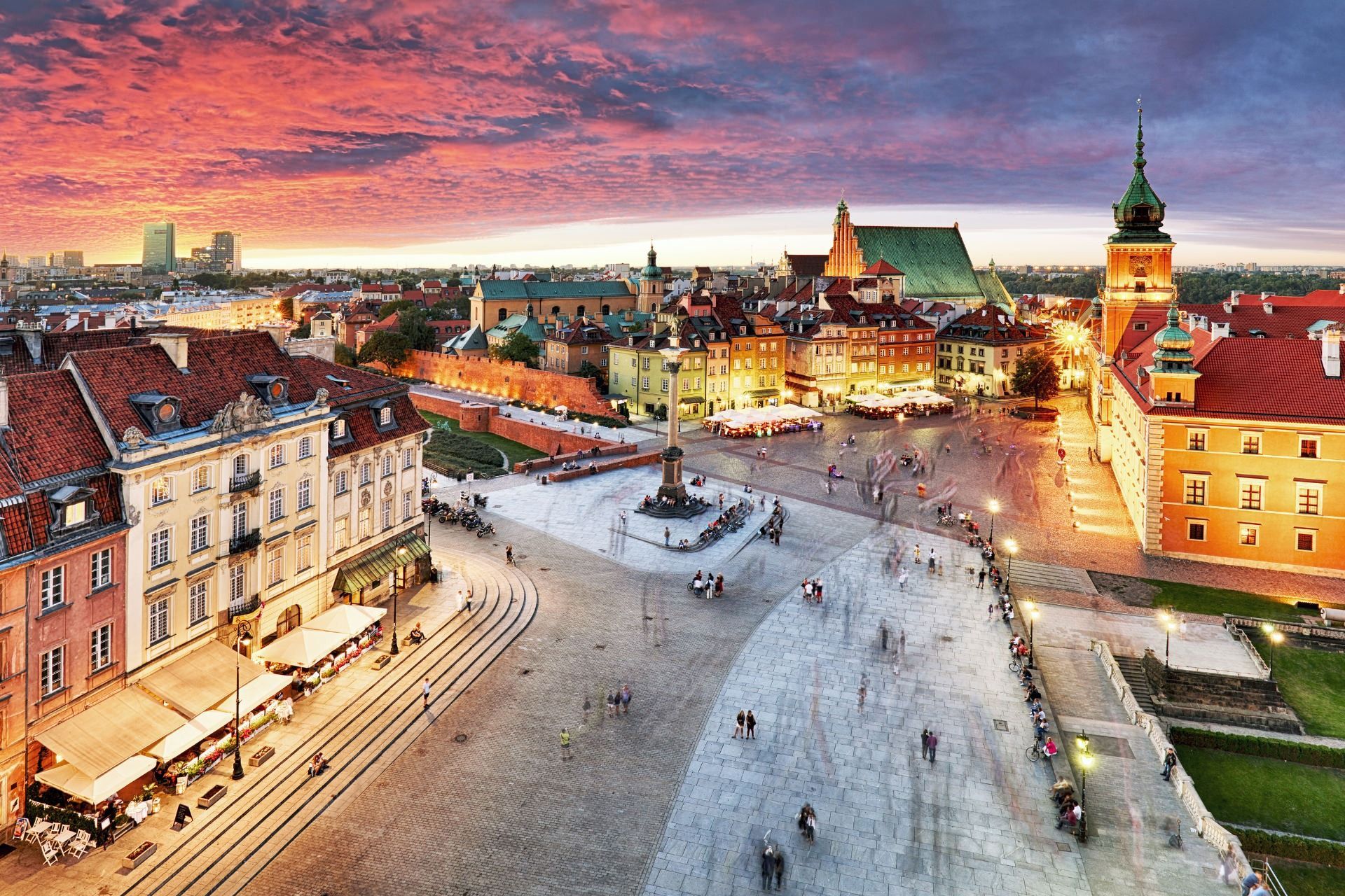 Aerial view of a European town square at sunset with red-roofed buildings and a church tower