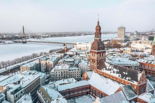 Snowy aerial view of a European city with a river, bridge, and church tower at sunset