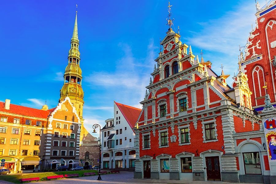 Colorful historic buildings and a tall church tower in a sunny European town square under a blue sky