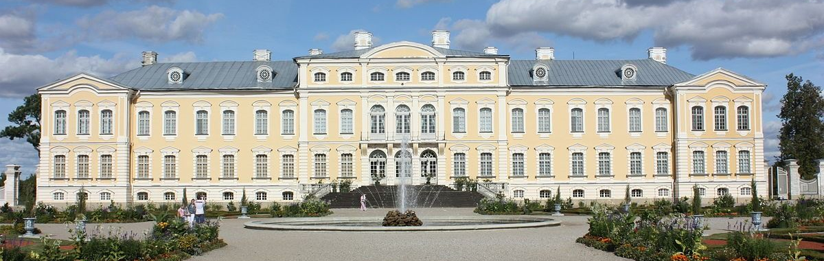 Grand pale-yellow historic palace with central stairs and gardens in front under a blue sky