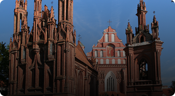 Gothic cathedral with tall spires framing a red brick church facade under a clear blue sky