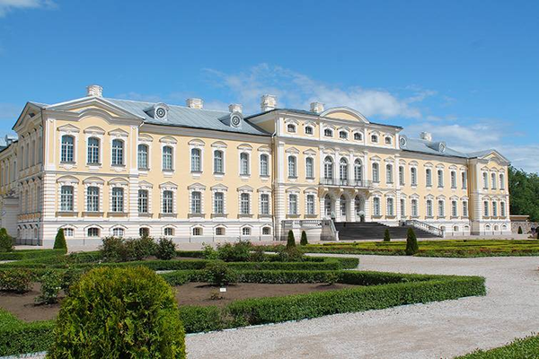 Grand white historic palace with ornate windows, blue roof, and manicured gardens under a clear sky