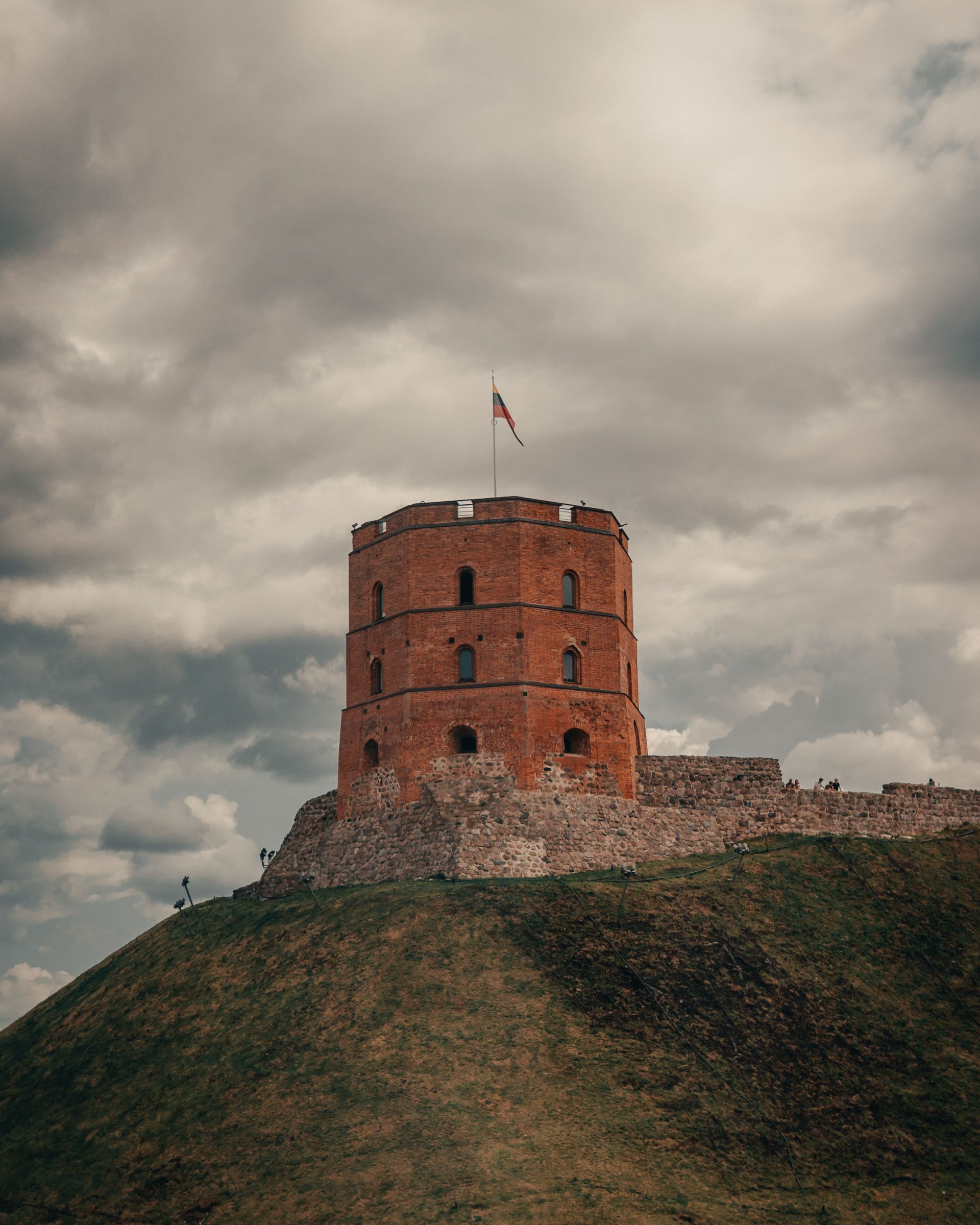 Round brick tower on a grassy hill under a cloudy sky with a bird flying overhead