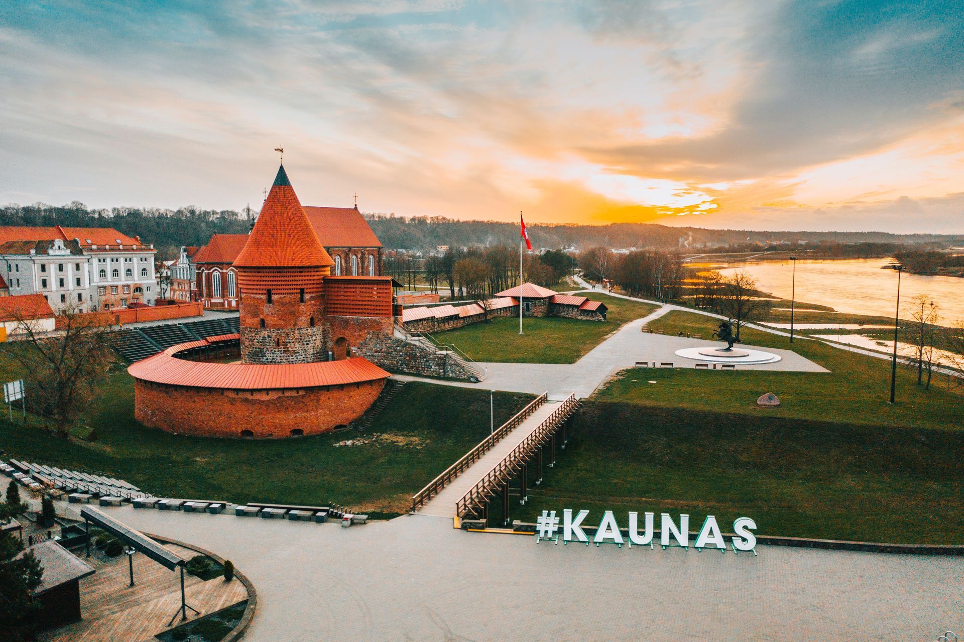 Kaunas riverfront at sunset with red brick castle and large #KAUNAS sign