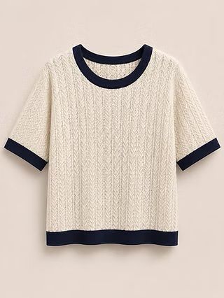 Camiseta de punto color crema con cuello, pu&ntilde;os y bajo azul marino sobre fondo liso.