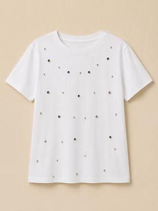 Camiseta blanca de manga corta con peque&ntilde;os puntos negros dispersos sobre un fondo beige.