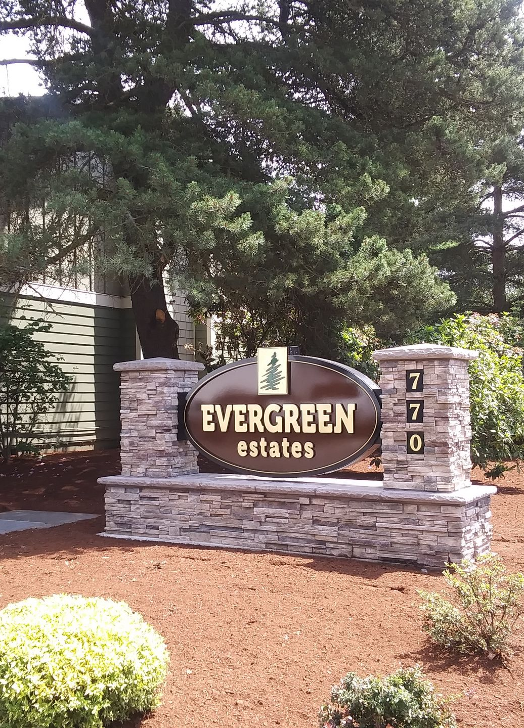 Evergreen Estates entrance sign with stacked stone base, surrounded by trees and shrubs.