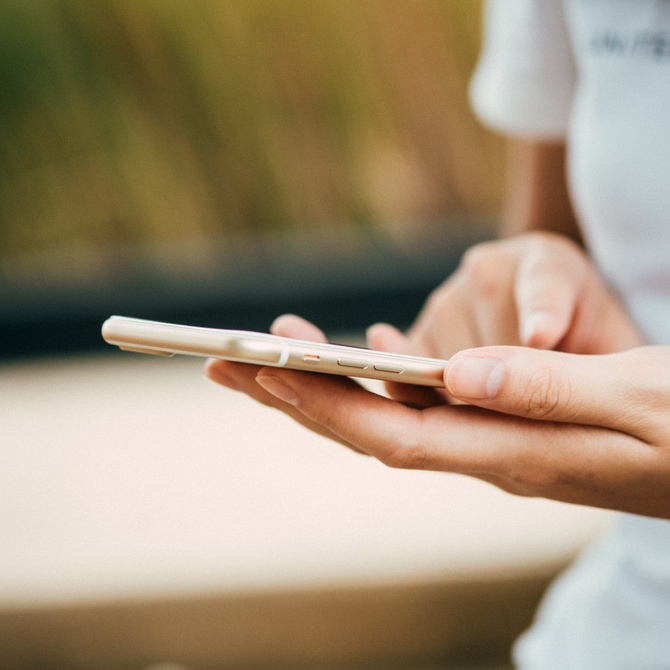Hands holding a smartphone outdoors with a blurred background