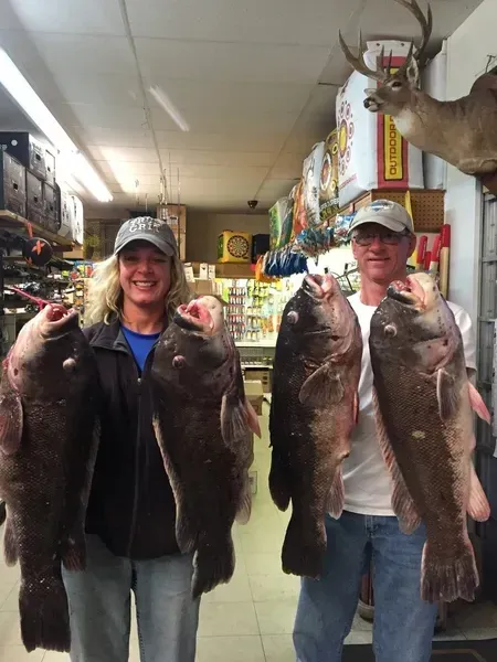 Two people holding up large dark fish, indoors near a deer head.