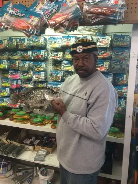 Man in a grey sweatshirt holds a large fish in a tackle shop.