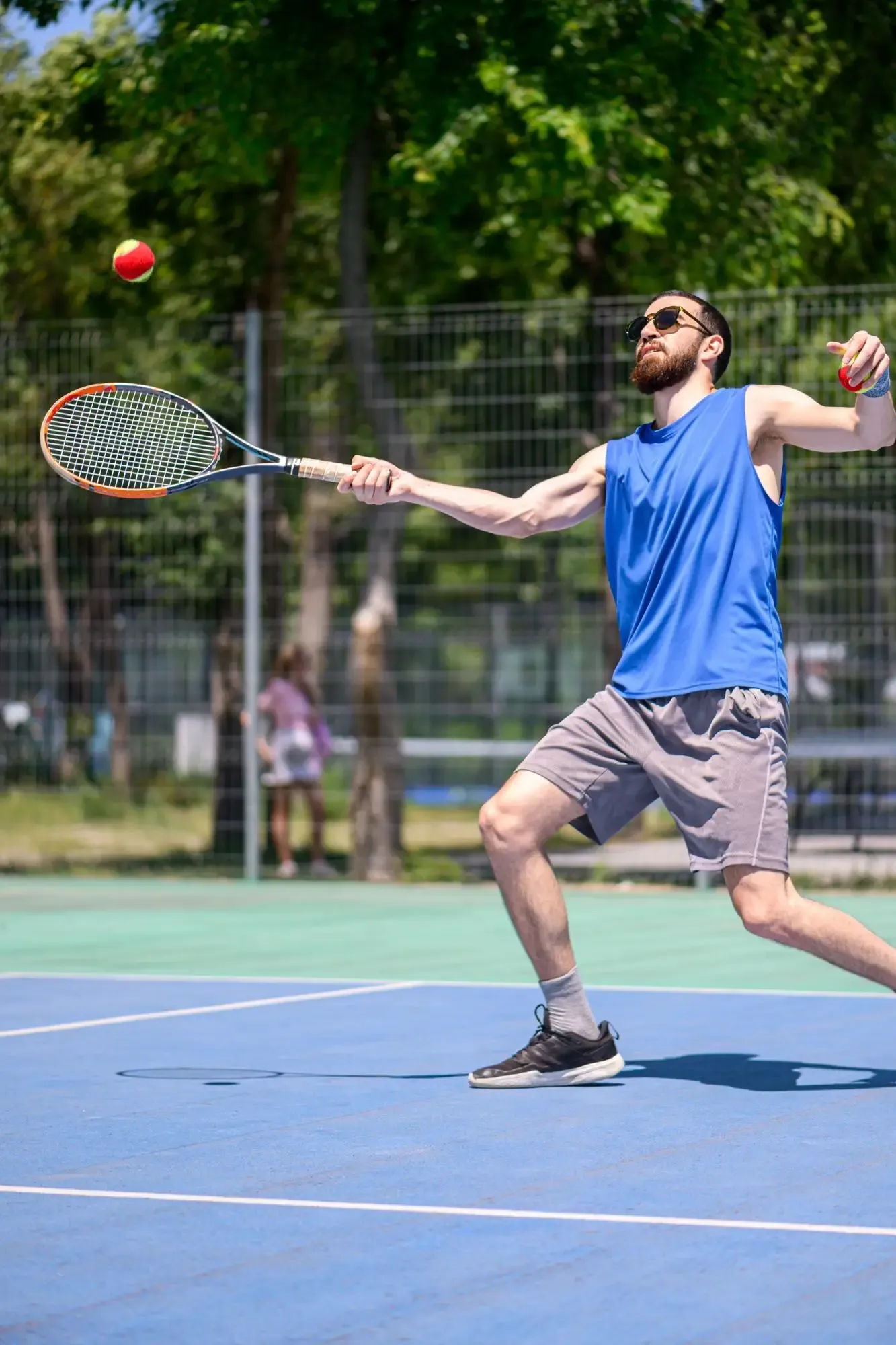 Tennis player in blue shirt reaching for a ball on an outdoor court.