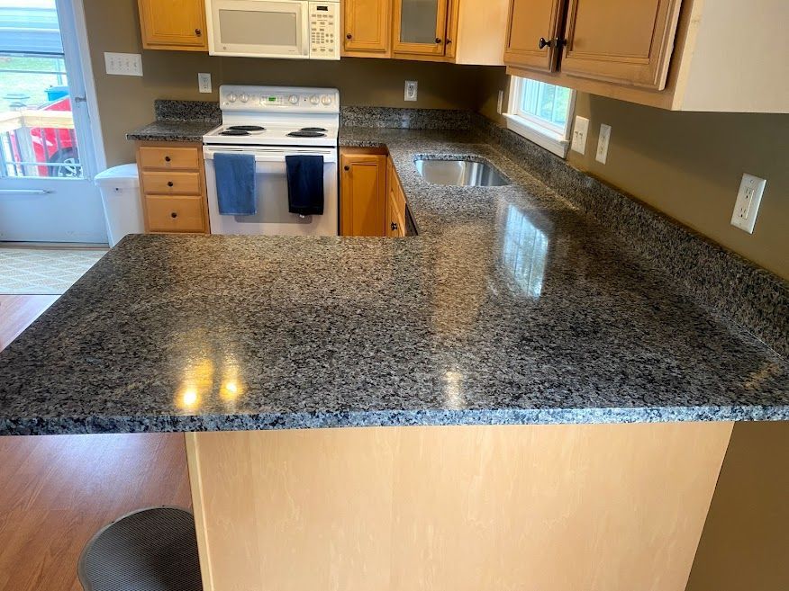 A kitchen with a granite counter top , stove , sink and microwave.