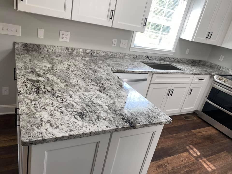 A kitchen with granite counter tops , white cabinets , a sink , and a stove.