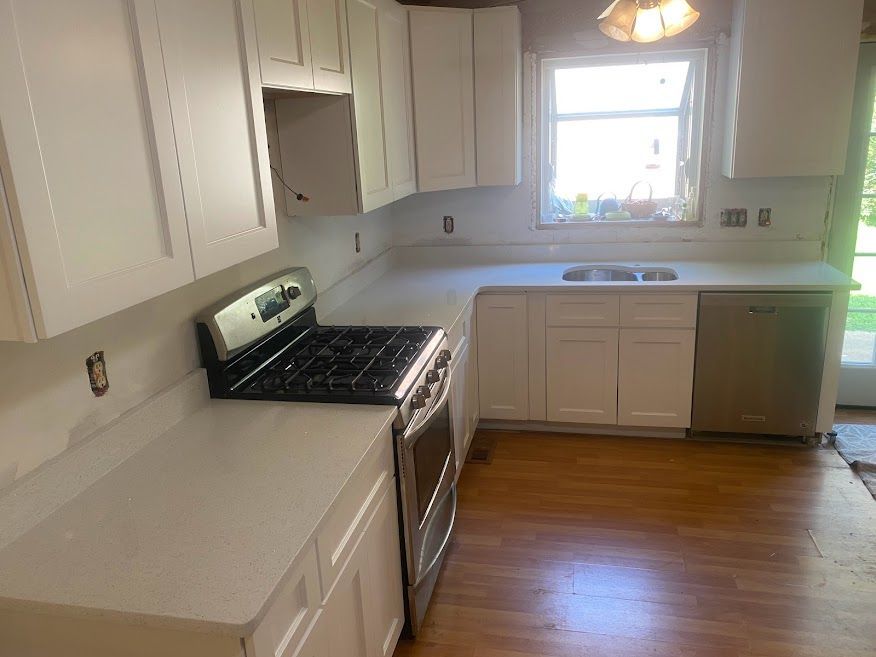 A kitchen with white cabinets , a stove , a sink , and a window.