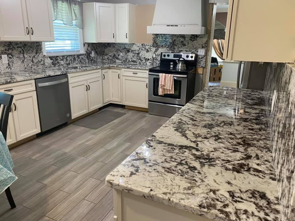 A kitchen with granite counter tops , stainless steel appliances , white cabinets and a stove.