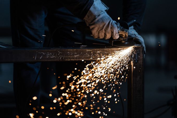 Un operaio smeriglia il metallo, proiettando scintille luminose in un'officina buia.