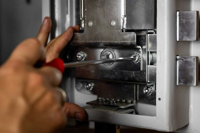 Mano che ruota un cacciavite rosso per regolare un meccanismo di chiusura metallico all'interno di un armadio.