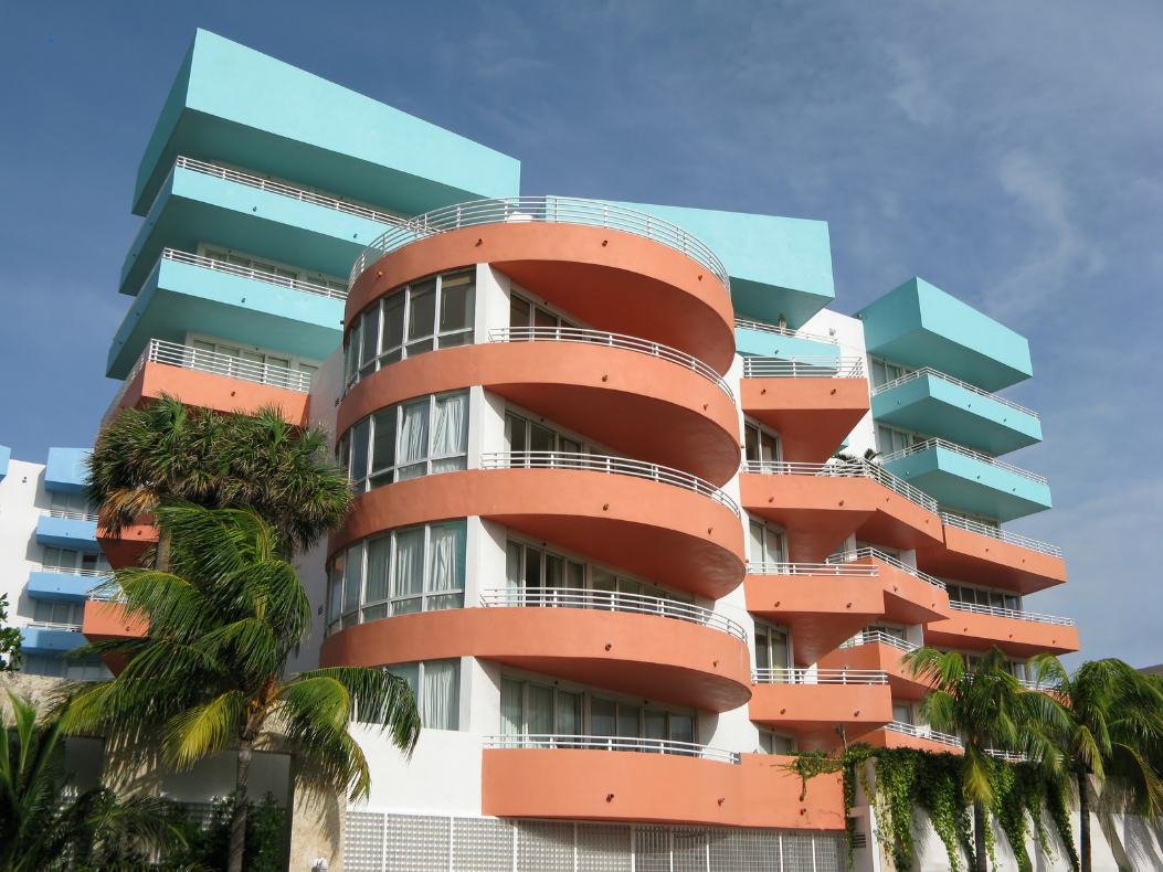 Modern multistory apartment building with turquoise balconies and coral curved terraces under a blue sky