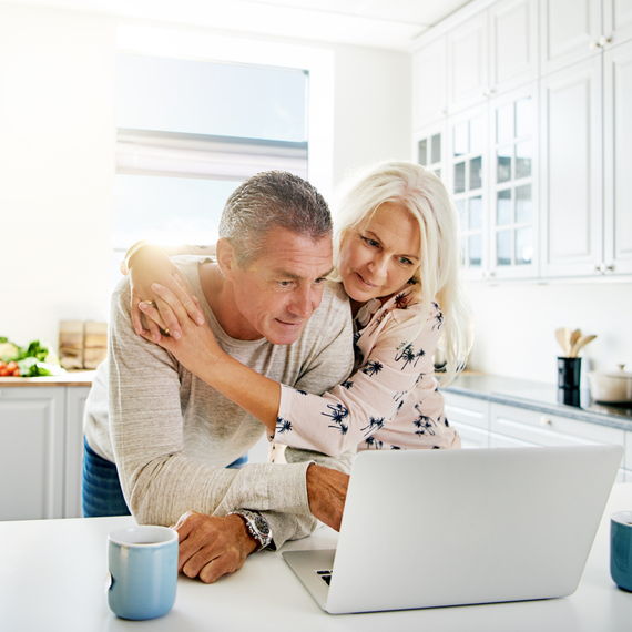 Two people embracing at a laptop in a bright kitchen, with a blue mug on the counter.