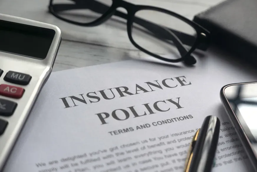 Insurance policy document with calculator, glasses, pen, and magnifying glass on a desk