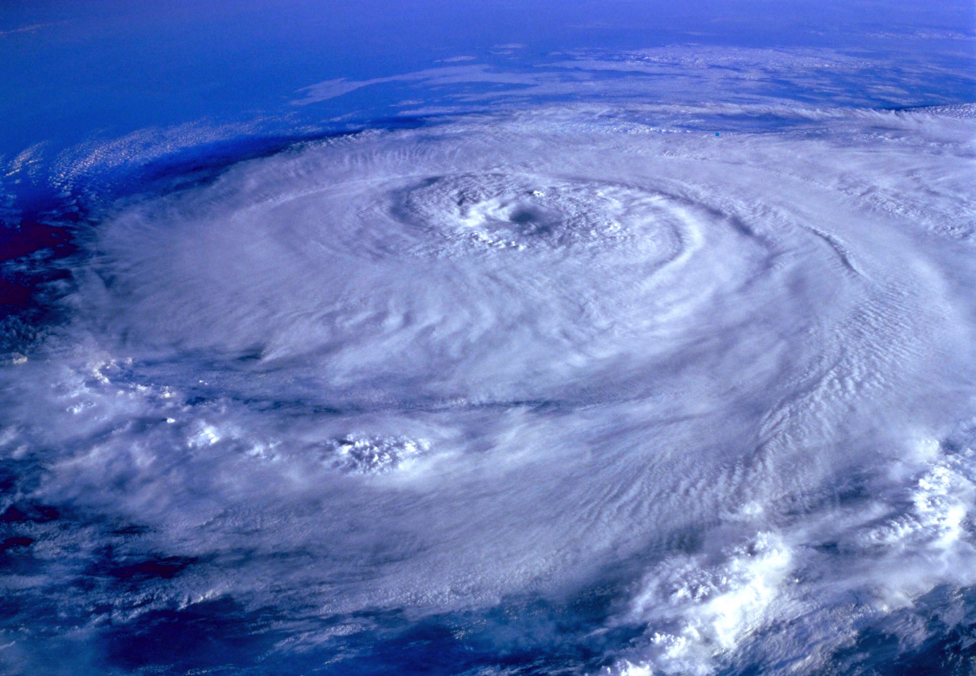 A massive swirling hurricane cloud over the ocean, viewed from above, with a clear eye at the center