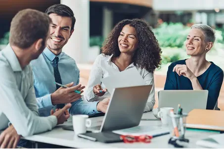 Colleagues smiling and talking around laptops in a bright office meeting space