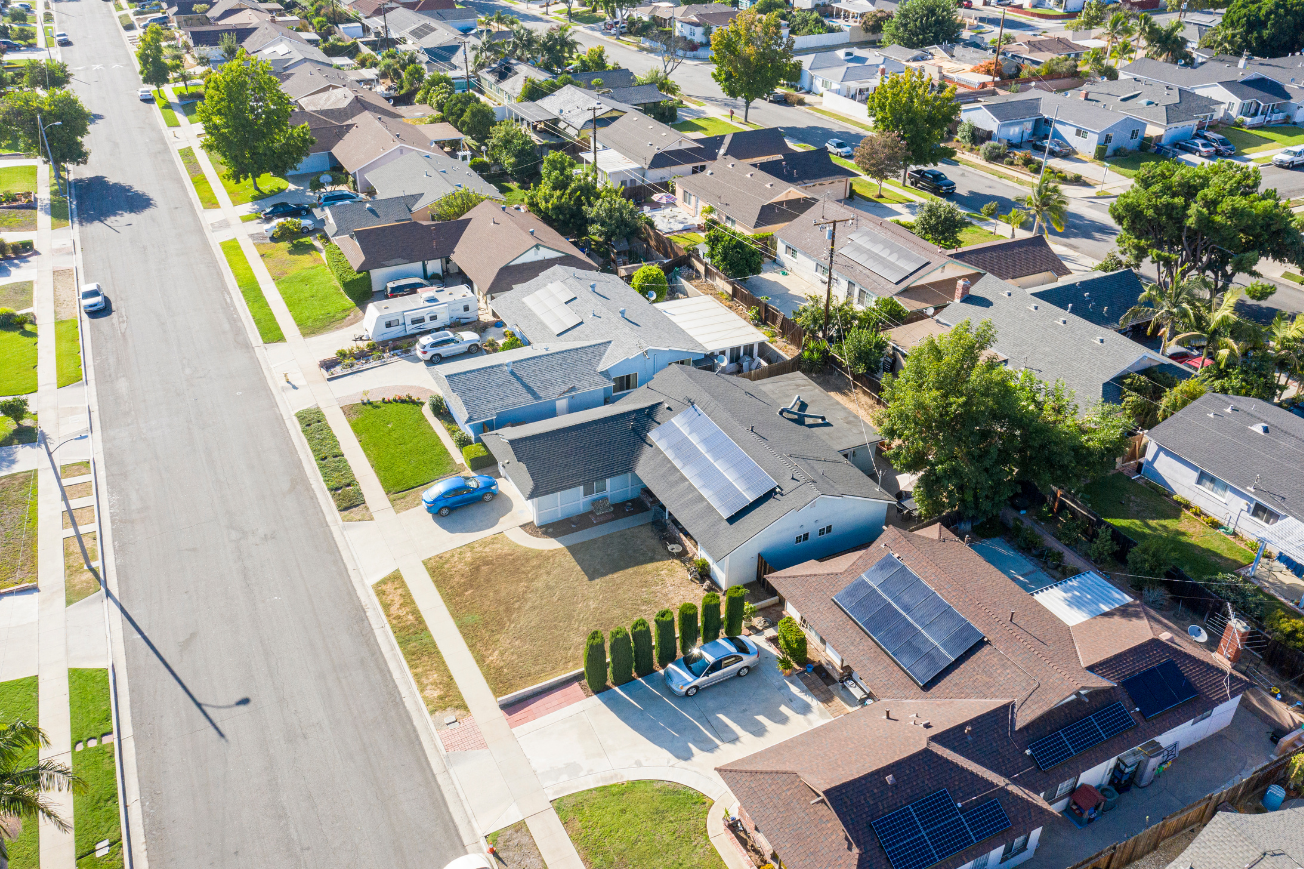 Aerial view of a quiet suburban neighborhood with houses, driveways, trees, and a road.