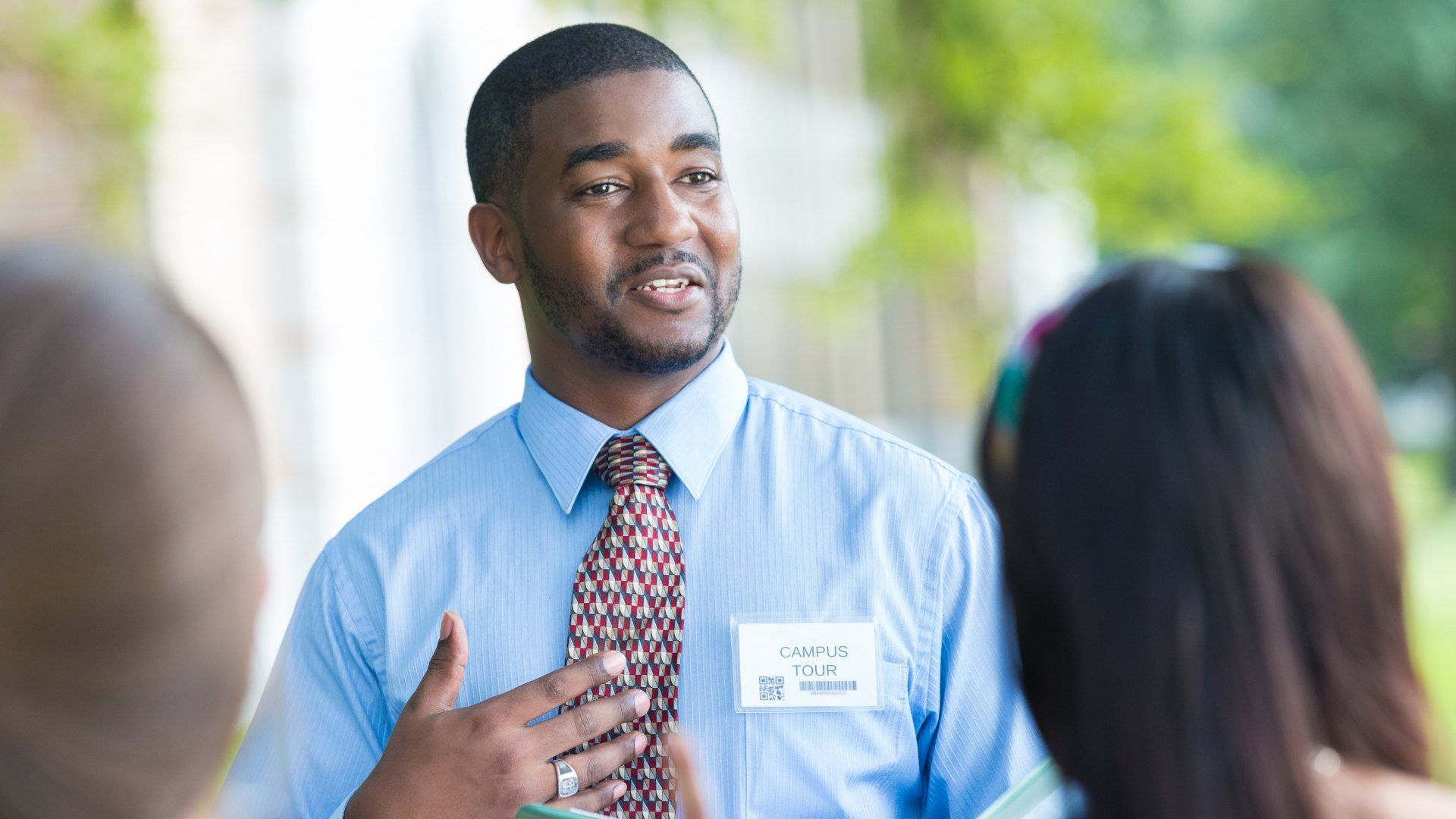 Man in a blue shirt and name badge talking with colleagues outdoors