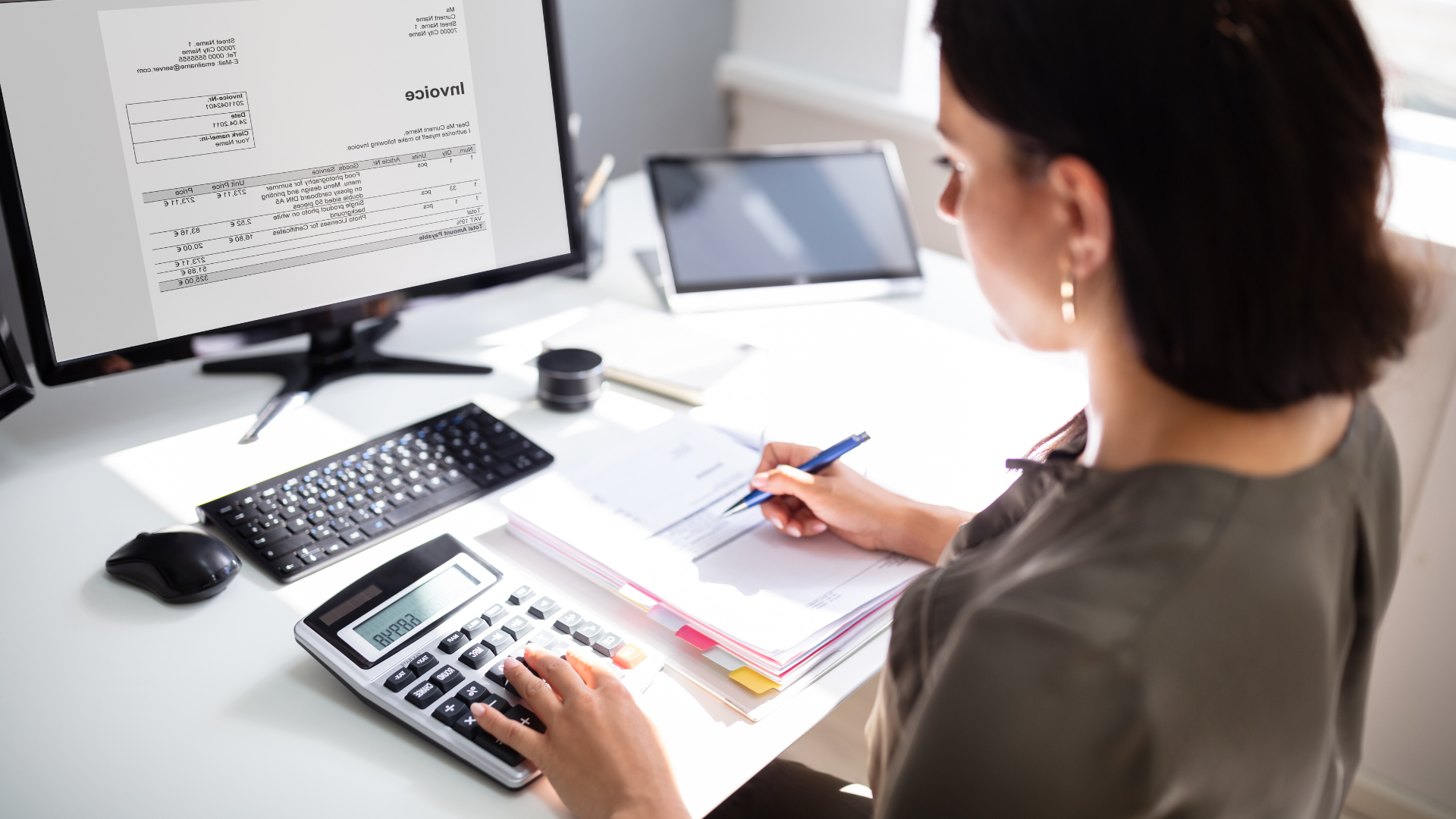 Woman using a calculator to review budget paperwork at a desk