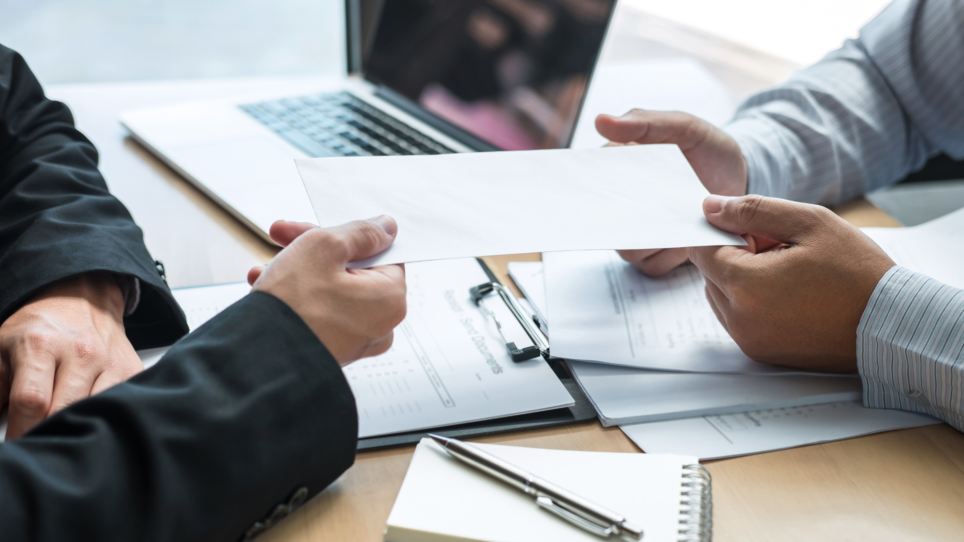 Businessperson handing a document across a desk during a meeting