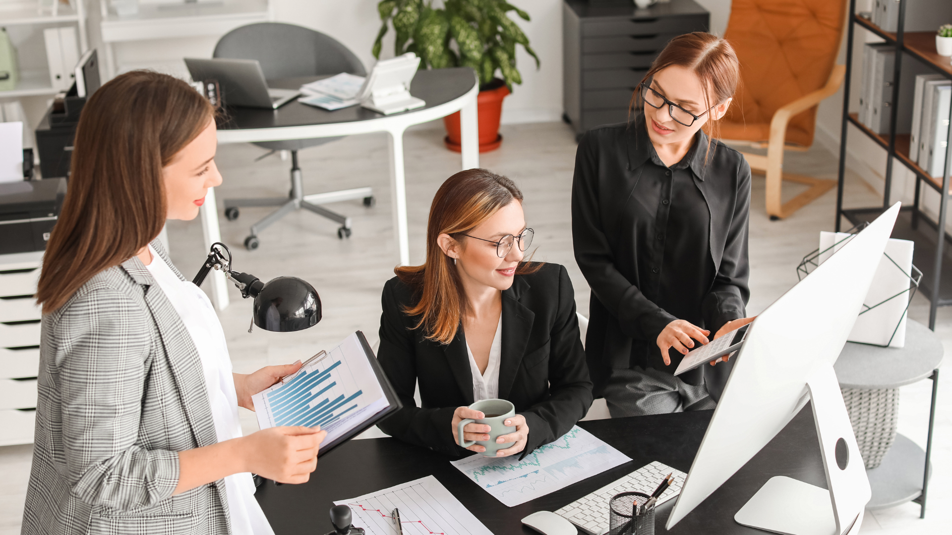 Three colleagues discussing financial charts around an office computer