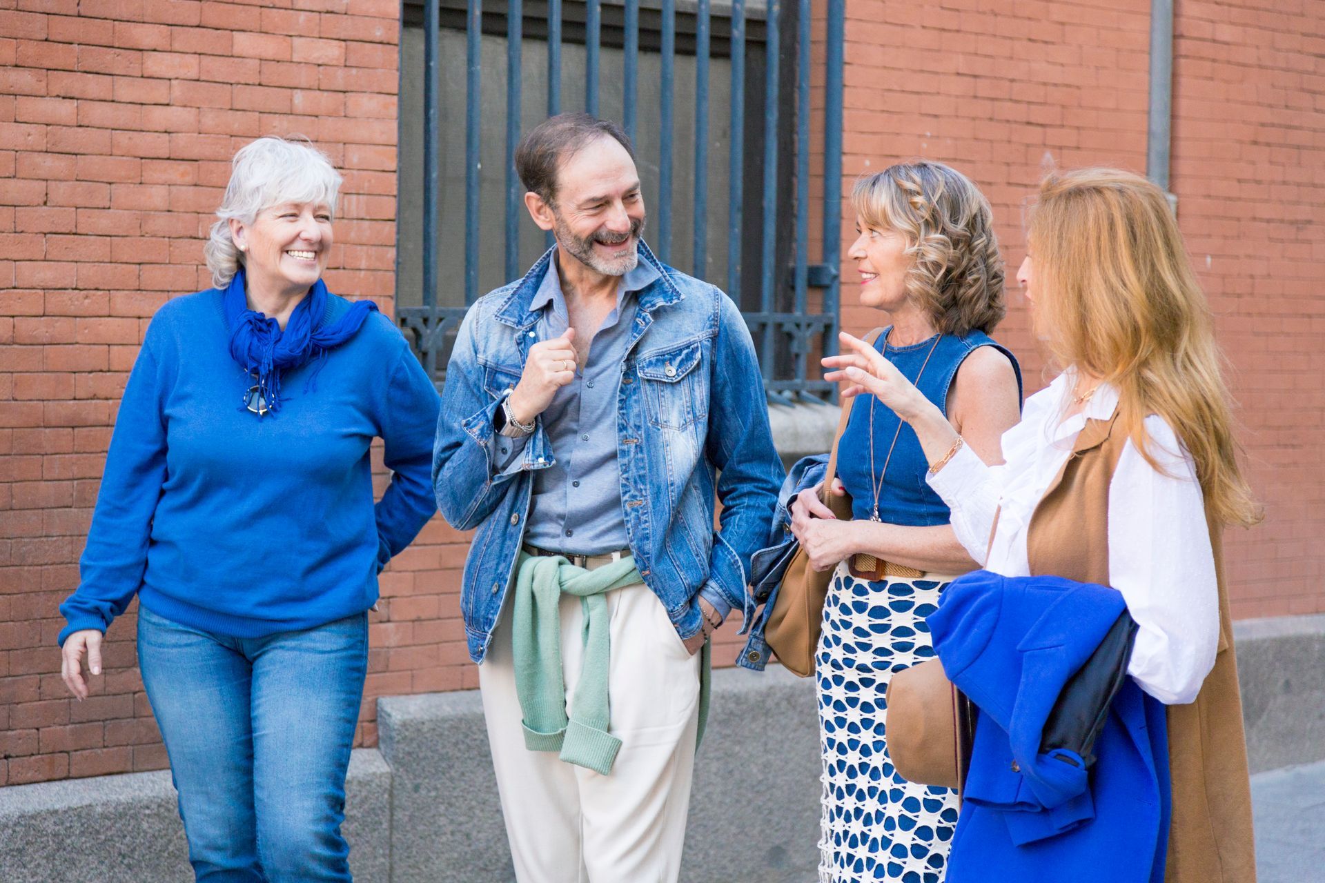 Four people chatting and smiling outside a brick building, wearing casual clothes and jackets