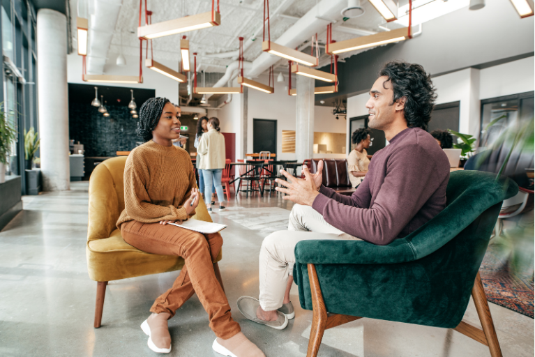 Two people talking in a bright modern office lounge with green and tan chairs