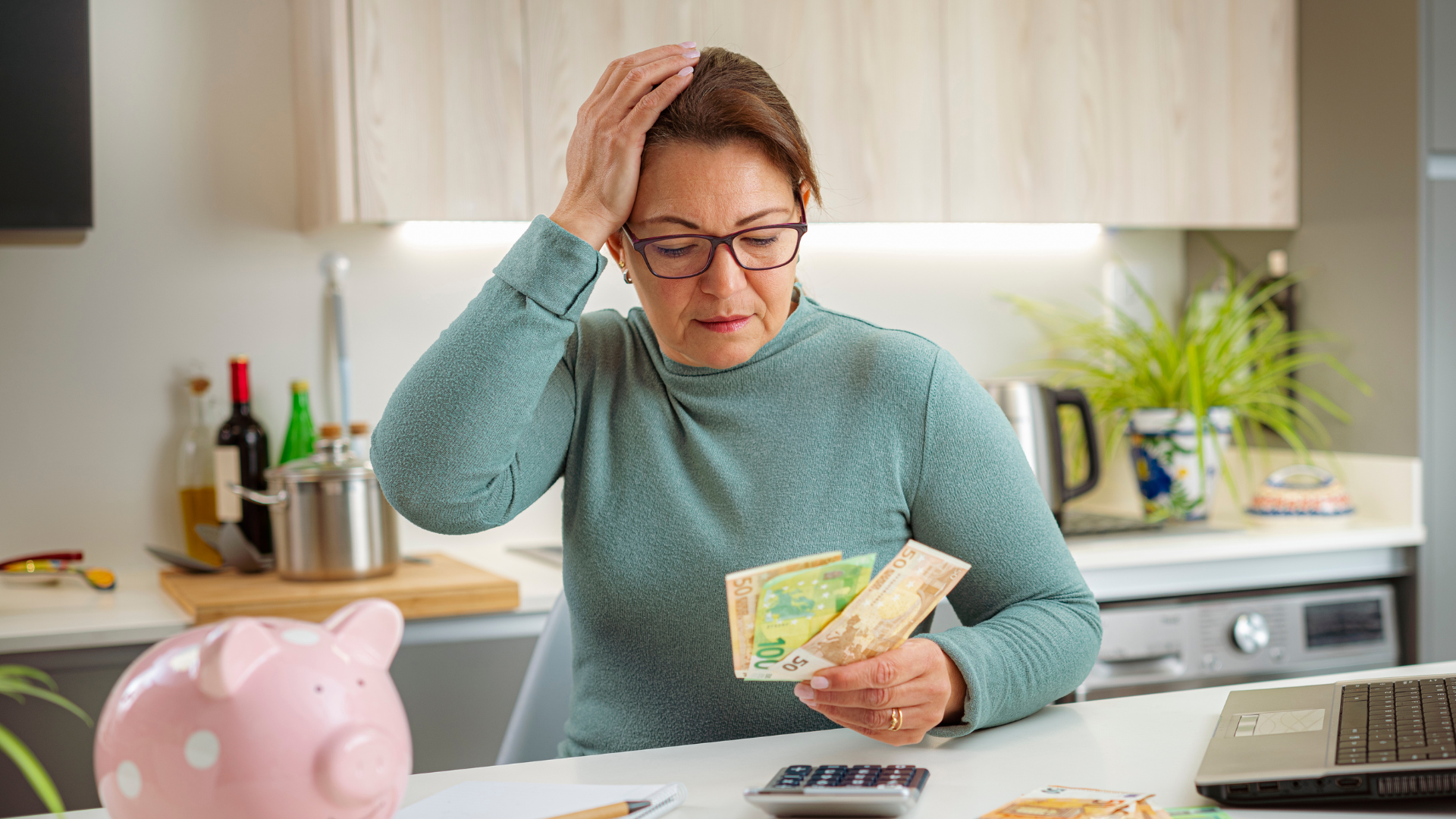 Worried woman holding cash next to a piggy bank while reviewing household costs