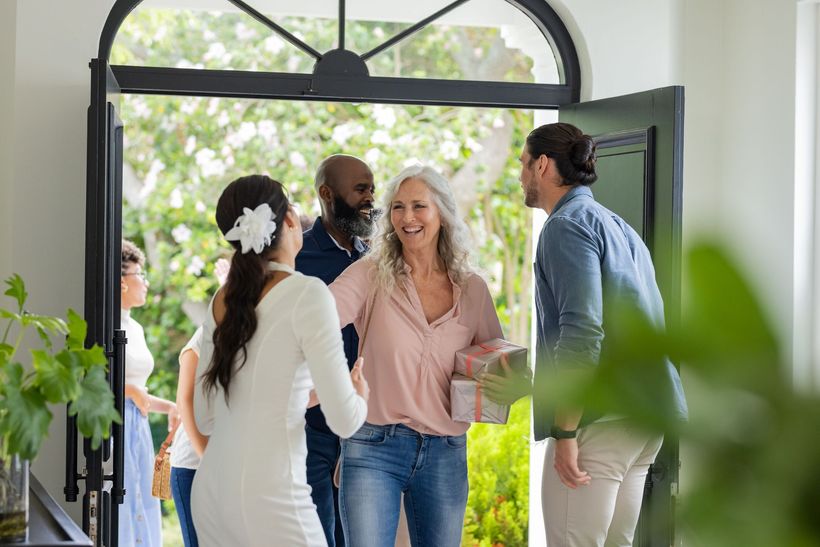 People greeting at a front doorway with open glass doors and greenery outside