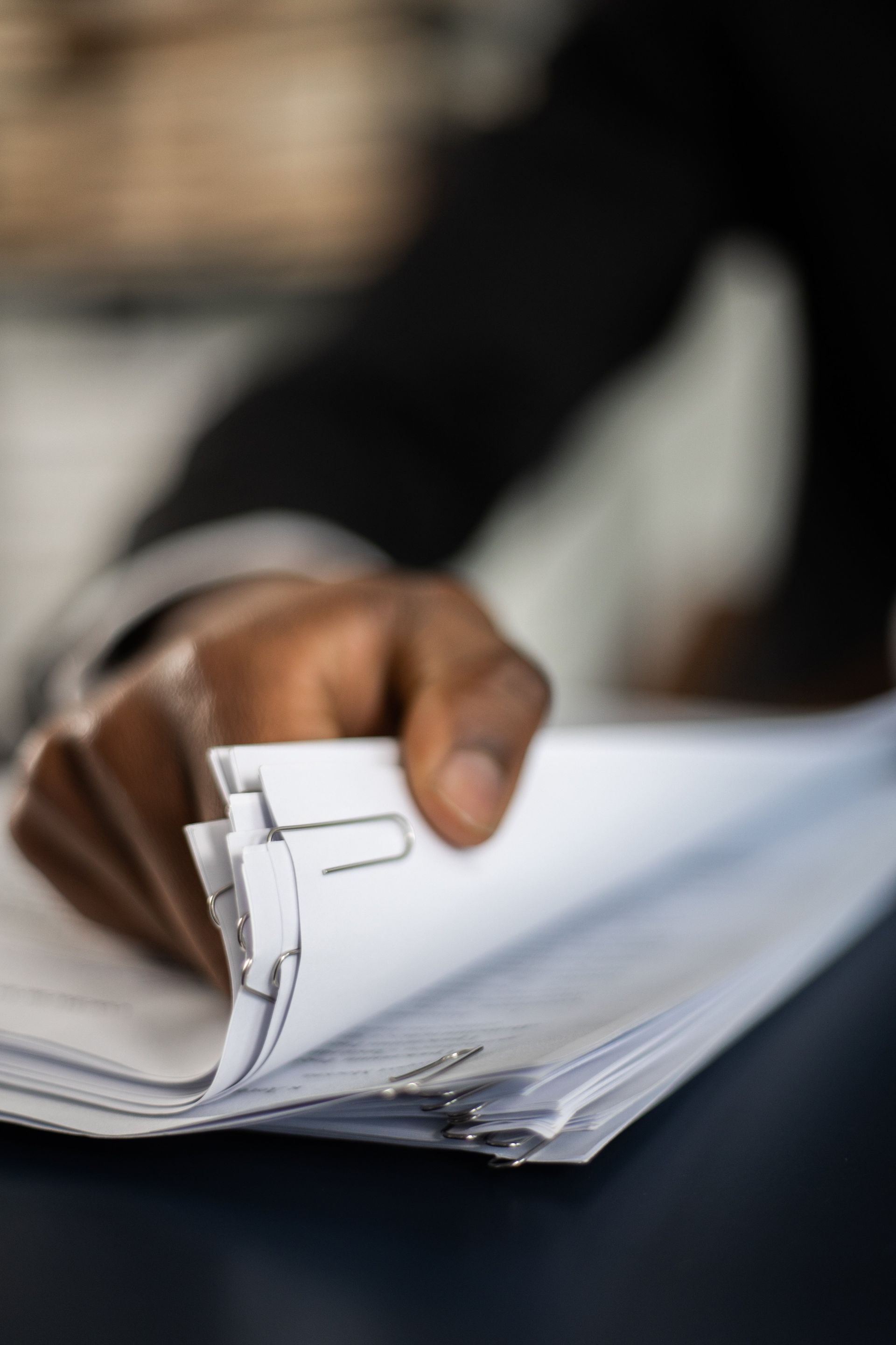 Hand turning a page in a stack of documents, with a paper chart visible on top.
