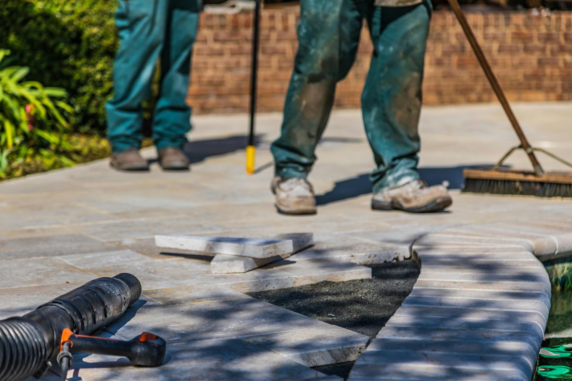 Workers installing paving stones on a curved patio with tools nearby