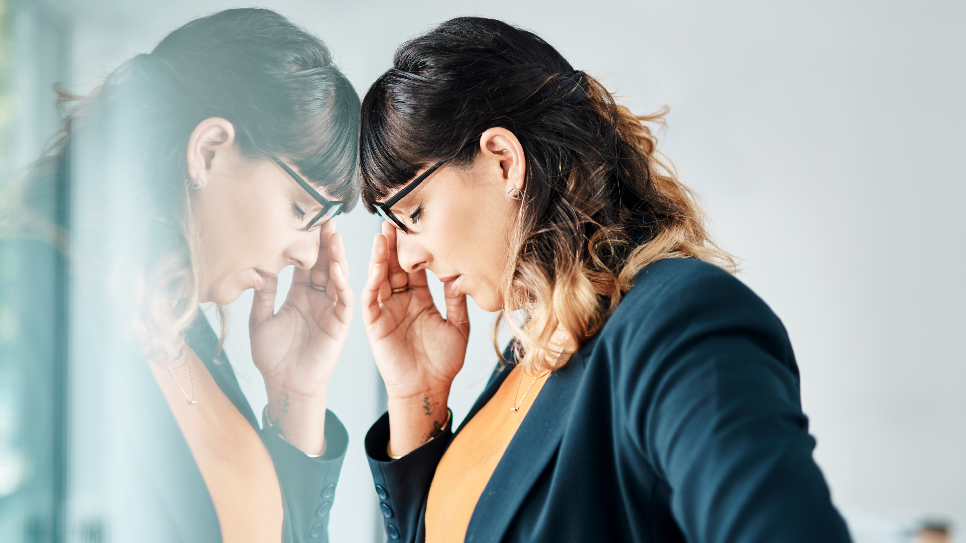 Stressed businesswoman leaning against a window with her reflection visible