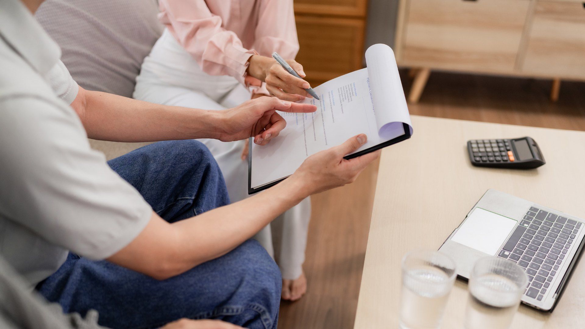Two people reviewing a document on a clipboard beside a calculator and laptop