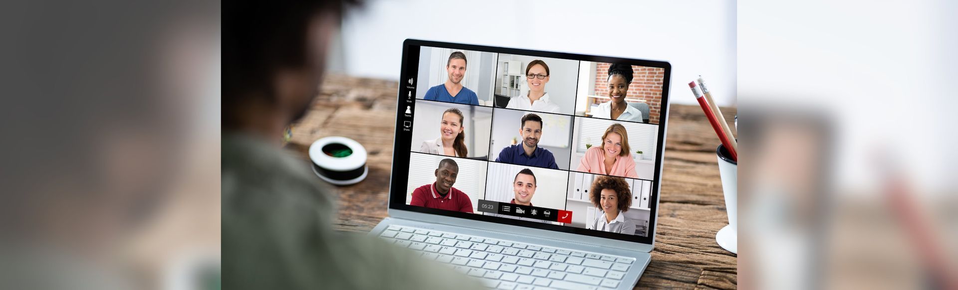 Video conference on a laptop showing a nine-person grid in a home office setting