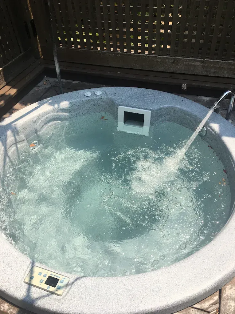 Round hot tub filled with bubbling water, viewed from above in a fenced outdoor area