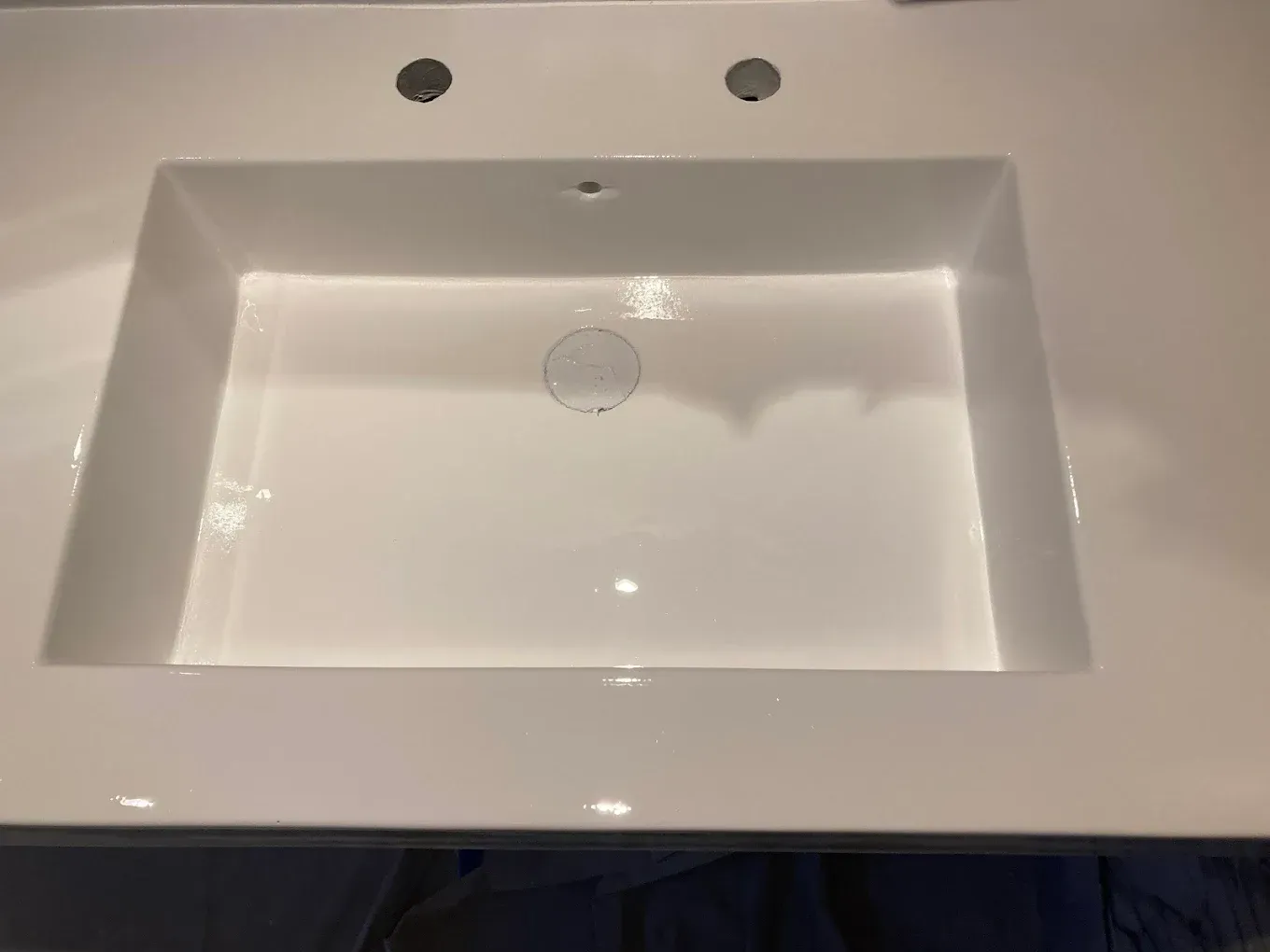White rectangular bathroom sink with three faucet holes and a round drain in the basin