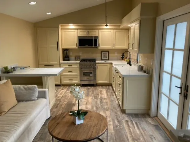 Modern beige kitchen and living area with island, sofa, round coffee table, and glass doors
